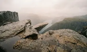 Trolltunga i Norge, en ikonisk klippa som skjuter ut över en fjord. En dramatisk vy med dimma som sveper över bergen.