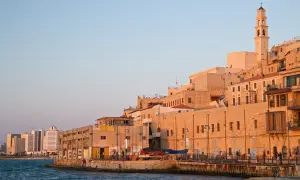 Gamla Jaffa i Tel Aviv badar i solnedgångens gyllene ljus. En klocktorn reser sig över de gamla stenbyggnaderna vid havet.