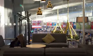 Mysig lounge med soffor, bord och lampor. En jacka hänger på en klädhängare. Utsikt över flygplatsen från Pearl Lounge Arlanda.