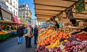 Frukt och grönsaksstånd på en livlig loppmarknad i Paris. Folk handlar bland färska druvor, apelsiner och tomater.