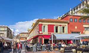 En livlig marknad i en nice gamla stan med färgglada byggnader, uteserveringar och folk som strosar.
