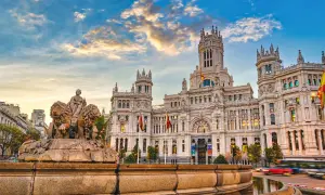 Cibelesfontänen framför det ståtliga Palacio de Comunicaciones, ett ikoniskt konstmuseum i Madrid, under en dramatisk solnedgång.