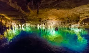 Magiska grottor på Mallorca med turkost vatten som reflekterar stalaktiter och stalagmiter. En båt anas i bakgrunden.