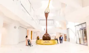 Imponerande chokladfontän i Lindt Home of Chocolate-museet. Familjer beundrar den gigantiska skulpturen i den ljusa, moderna byggnaden.