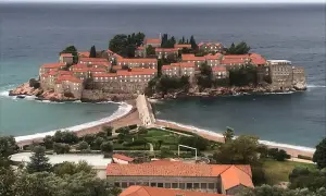 Sveti Stefan, en pittoresk ö med stenhus och röda tak, förbunden med fastlandet via en smal landremsa.