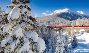 Röda tåget korsar en snöig bro i Schweiz, ett drömresmål med majestätiska berg och vinterlandskap.