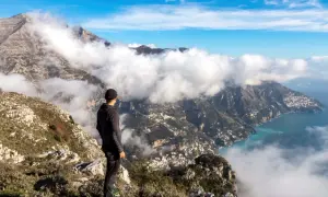 Vandrare på gudarnas stig blickar ut över moln som sveper in en kuststad vid havet.