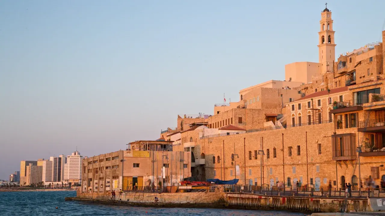 Gamla Jaffa i Tel Aviv badar i solnedgångens gyllene ljus. En klocktorn reser sig över de gamla stenbyggnaderna vid havet.
