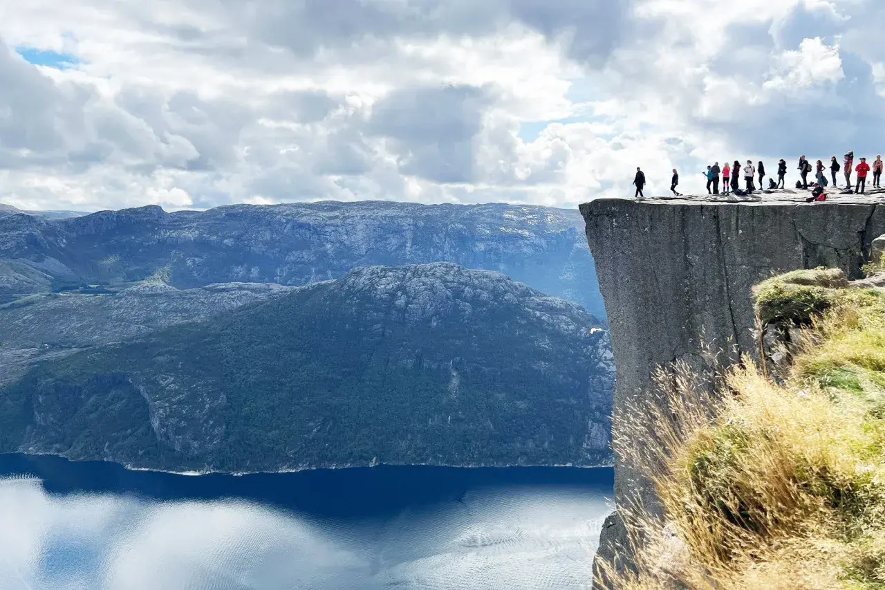 En grupp människor står på kanten av Preikestolen i Norge, med en dramatisk utsikt över fjord och berg.