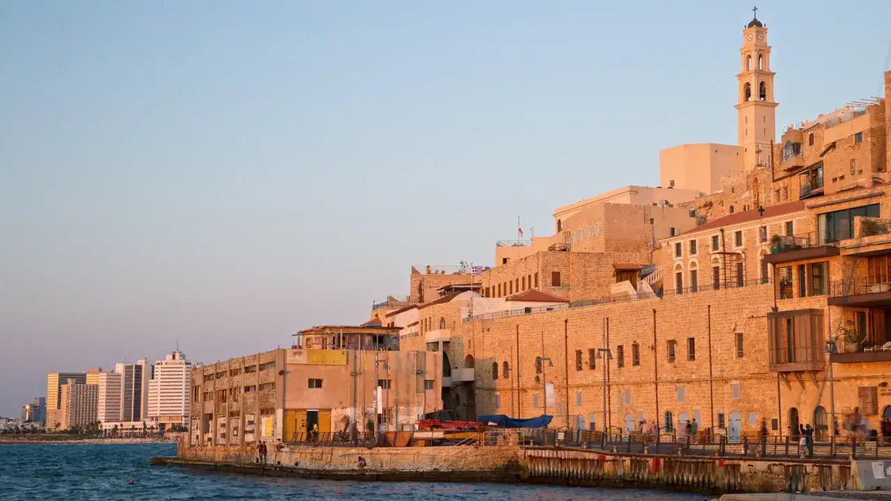 Gamla Jaffa i Tel Aviv badar i solnedgångens gyllene ljus. En klocktorn reser sig över de gamla stenbyggnaderna vid havet.