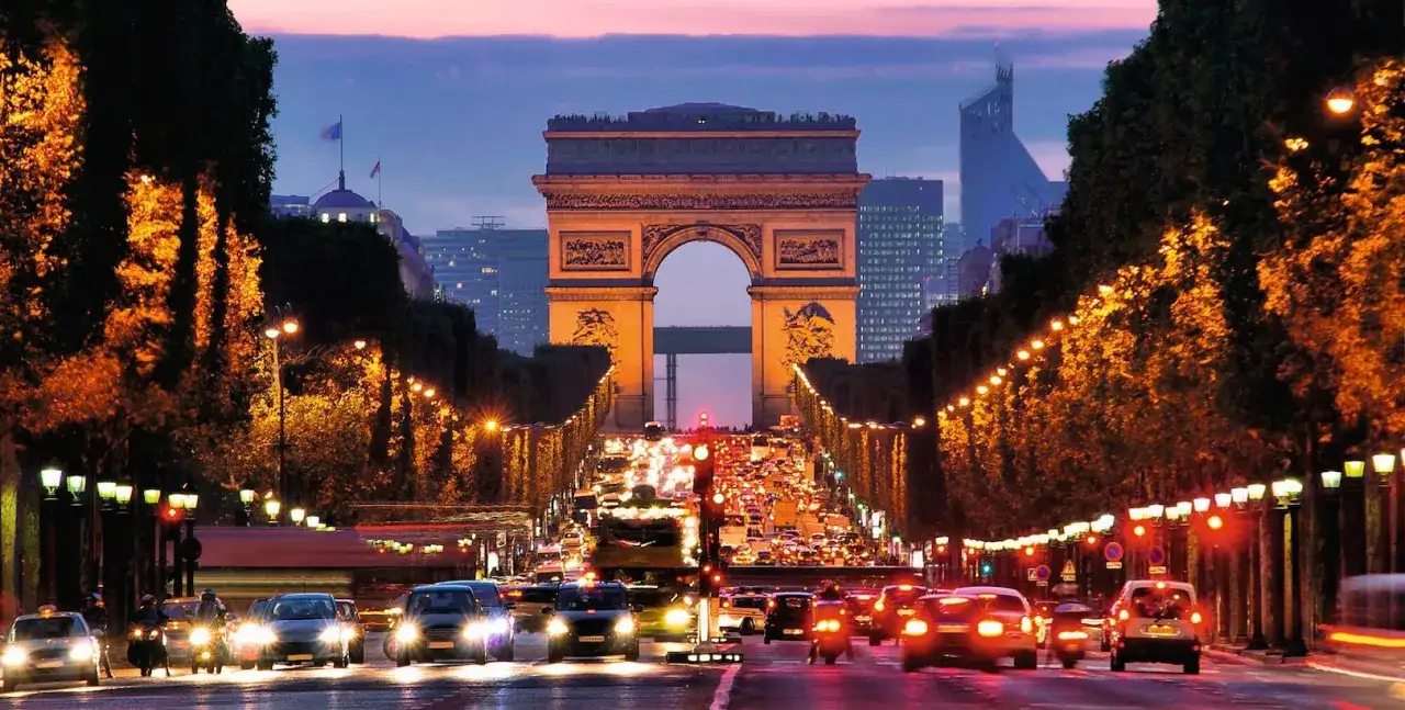 Trafikkaos vid Triumfbågen i Paris, en klassisk vy av saker att göra i Paris. Gatlyktor längs Champs-Élysées lyser upp kvällen.