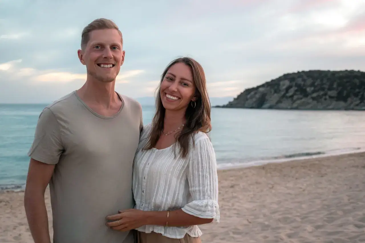 Ett lyckligt par njuter av solnedgången på en strand. De hittade dessa billiga resmål i Europa och delar ett romantiskt ögonblick.