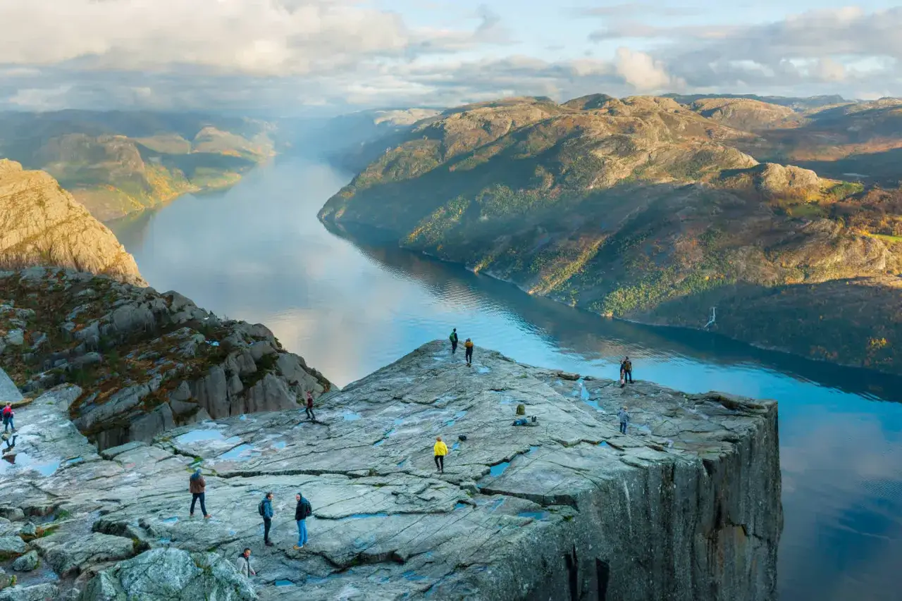 Vandrare njuter av den dramatiska utsikten från Preikestolen i Norge, med en djup fjord och bergiga landskap som sträcker sig bortom.