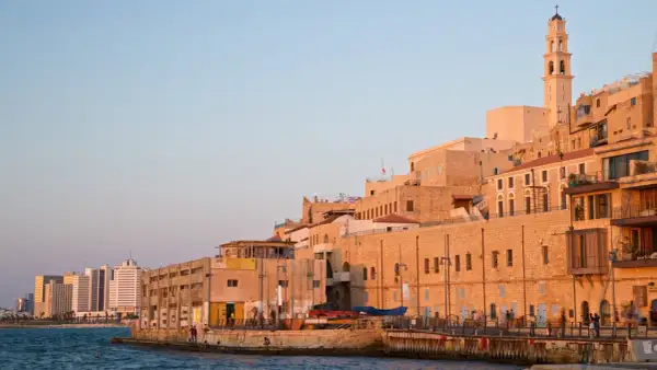 Gamla Jaffa i Tel Aviv badar i solnedgångens gyllene ljus. En klocktorn reser sig över de gamla stenbyggnaderna vid havet.