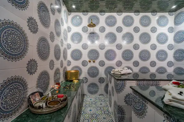 Ett vackert hammam i Marrakech med traditionella mönster på väggarna och golvet. En gyllene skål och skönhetsprodukter står redo för en avkopplande upplevelse.