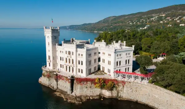 Vitt slott vid havet i Trieste, Italien, med en italiensk flagga på tornet.