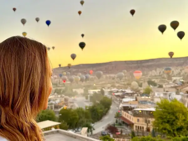 Kvinna ser på en magisk soluppgång över Kappadokien, Turkiet, med hundratals luftballonger som svävar i den gyllene himlen.