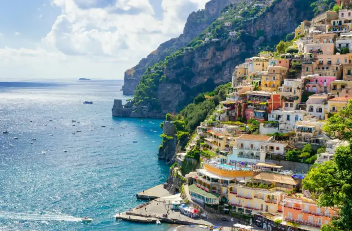 Färgstarka hus klättrar uppför en brant sluttning vid havet, ett drömresmål i Europa. Båtar guppar i det turkosa vattnet.