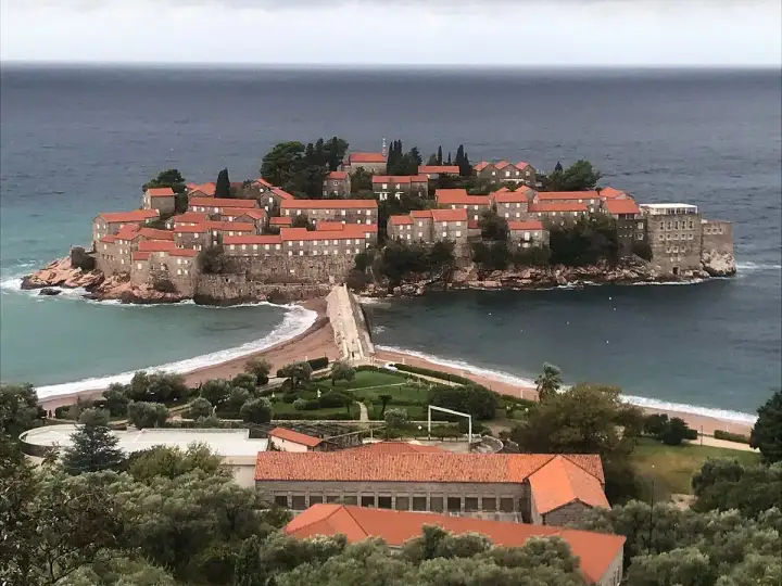 Sveti Stefan, en pittoresk ö med stenhus och röda tak, förbunden med fastlandet via en smal landremsa.